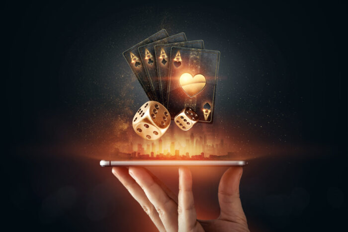 Creative background, online casino, in a man's hand a smartphone with playing cards, roulette and chips, black-gold background. Internet gambling concept. Copy space